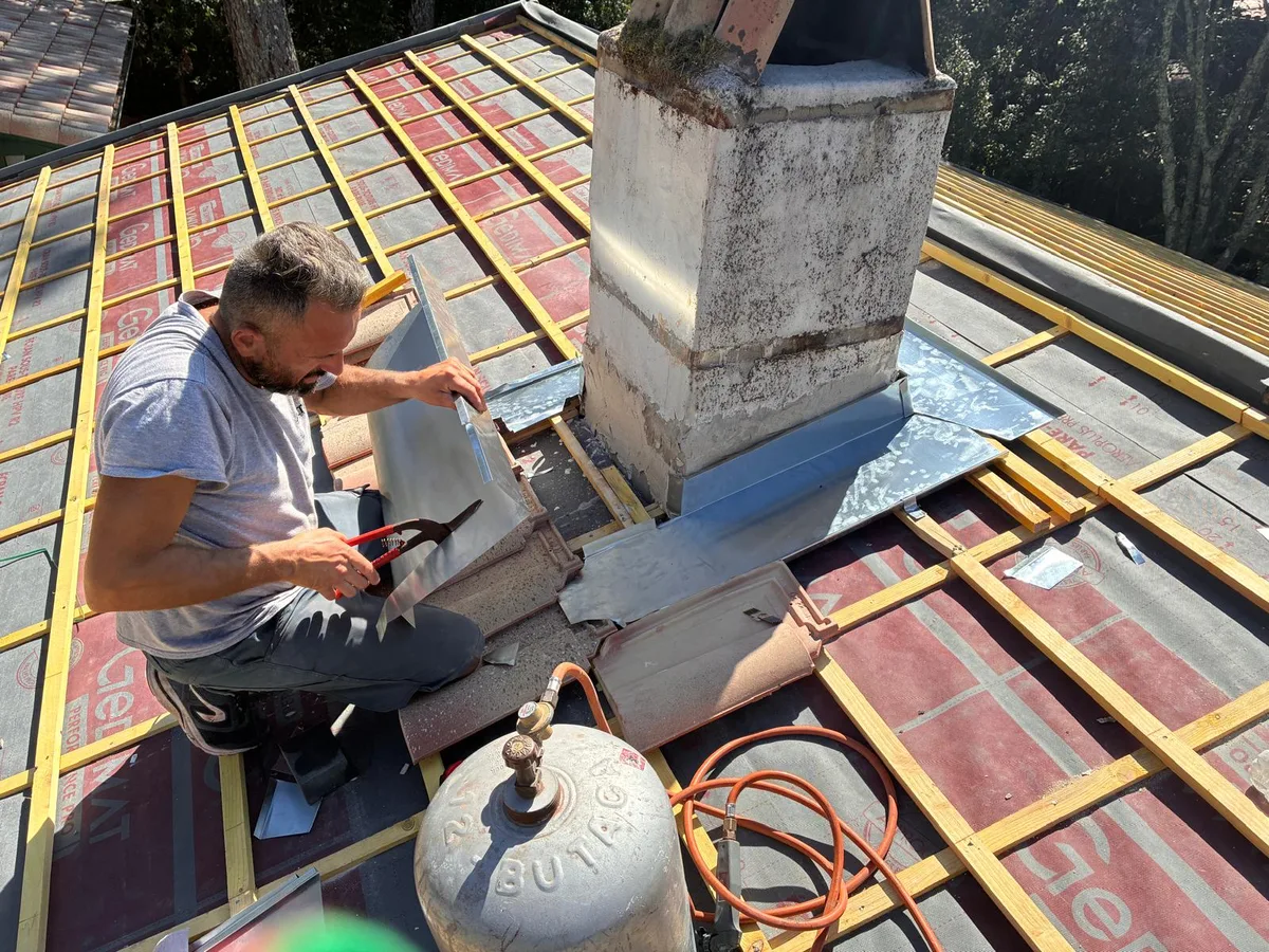 Couvreur travaillant le zinc au pied d’une cheminée, sur une toiture avec écran et liteaux
